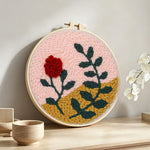 Red flower and green leaves punch needle artwork displayed on a table