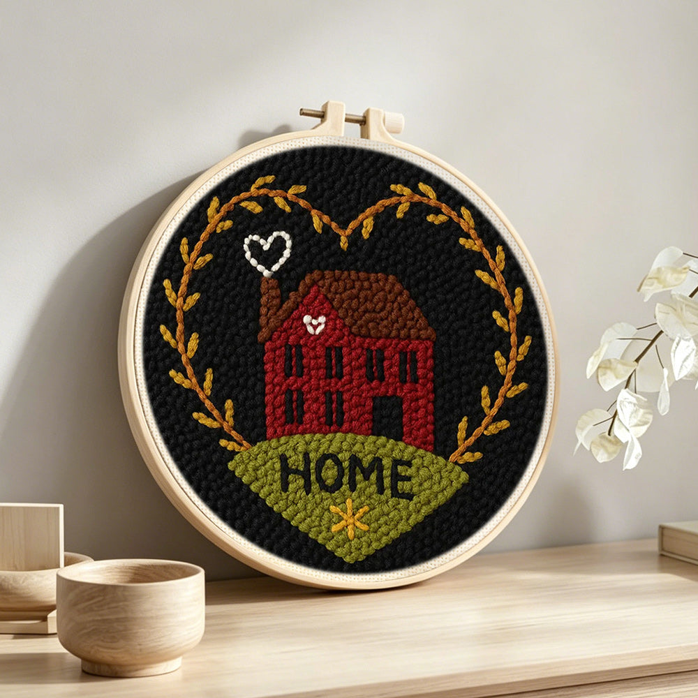 Red house with “home” heart wreath punch needle artwork displayed on a table