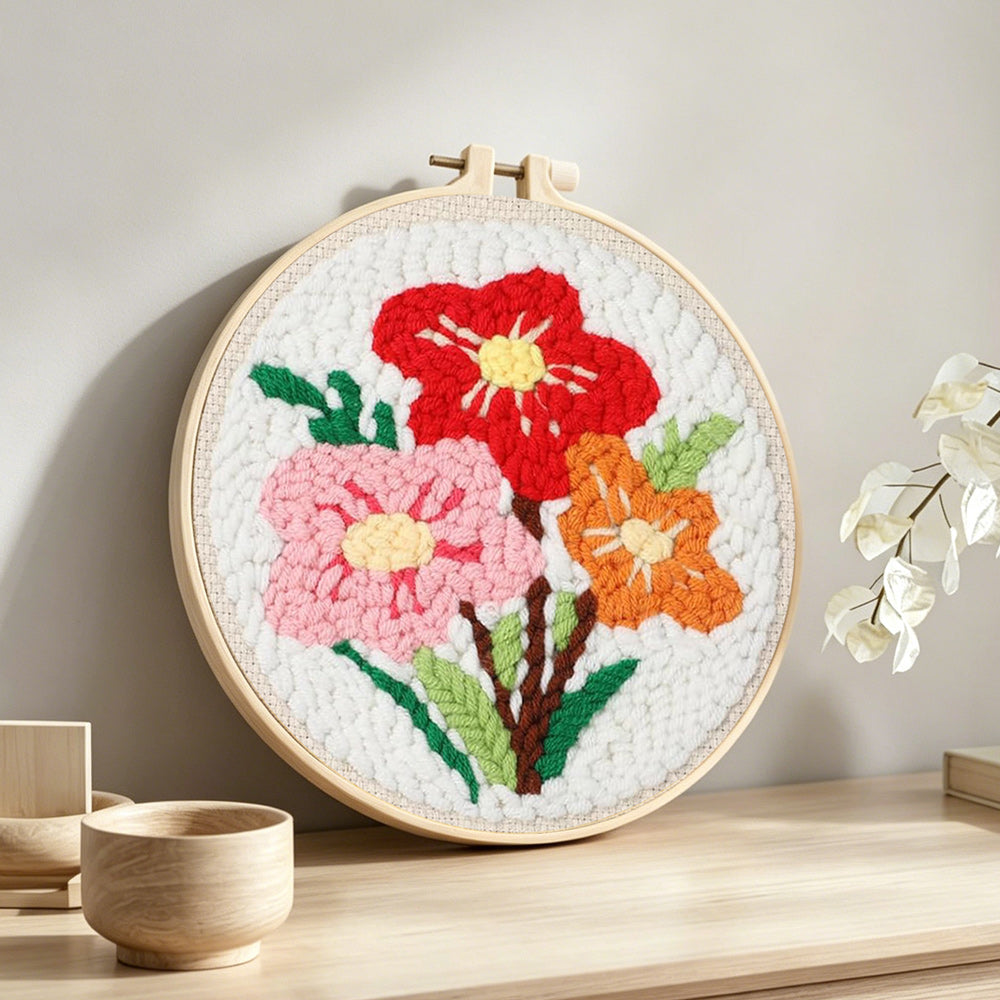 Red, pink and orange floral bouquet punch needle artwork displayed on a table