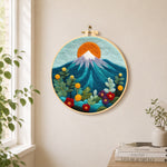 Red sun over snowy peaks needle felt wall art displayed in a bright home interior
