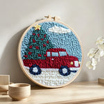 Red truck hauling christmas tree punch needle artwork displayed on a table