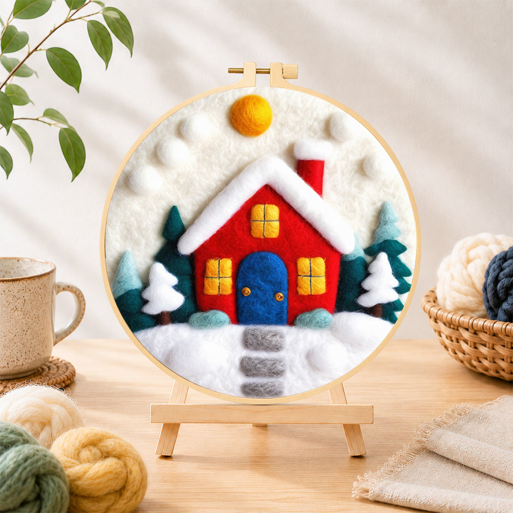 Finished red winter house with blue door needle felting displayed on a wooden easel