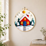 Red winter house with blue door needle felt wall art displayed in a bright home interior