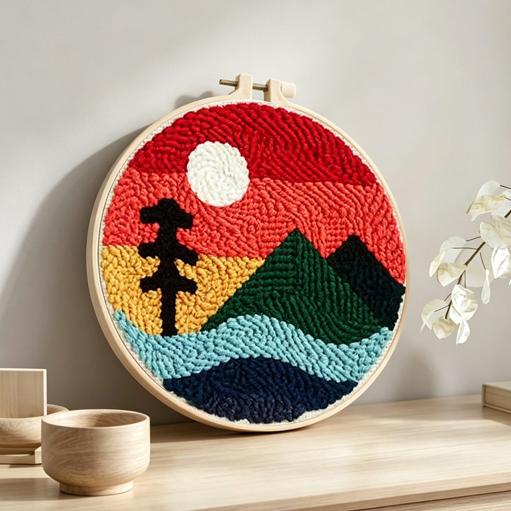 Ree and green mountain under red sky punch needle artwork displayed on a table