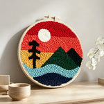 Ree and green mountain under red sky punch needle artwork displayed on a table