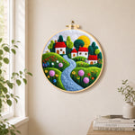 Serene blue river and red roof village needle felt wall art displayed in a bright home interior