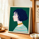 Short curly hair woman with green striped sweater punch needle artwork displayed on a table