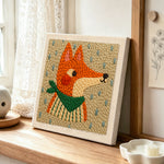 Side-profile fox with green scarf punch needle artwork displayed on a table