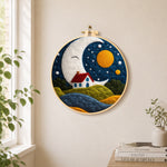 Smiling giant moon and little red cottage needle felt wall art displayed in a bright home interior