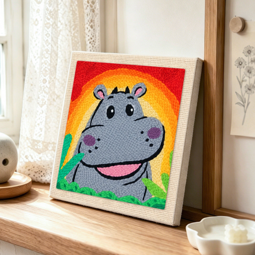 Smiling grey hippo with rainbow sunset punch needle artwork displayed on a table