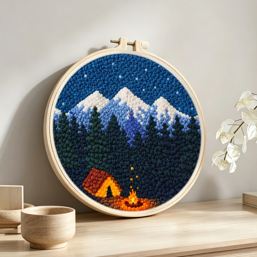 Snow-capped mountains, dark forest and campfire punch needle artwork displayed on a table