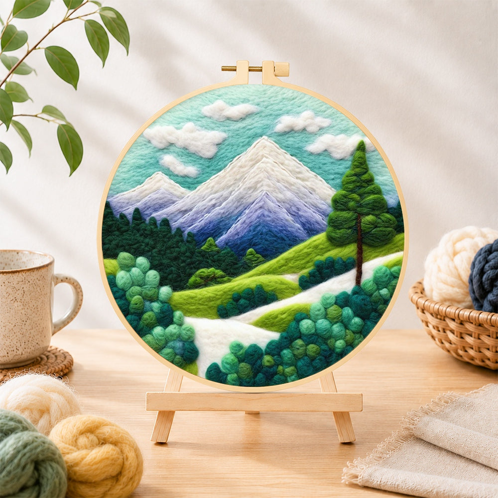 Finished snow-capped peaks and green trees needle felting displayed on a wooden easel