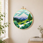 Snow-capped peaks and green trees needle felt wall art displayed in a bright home interior