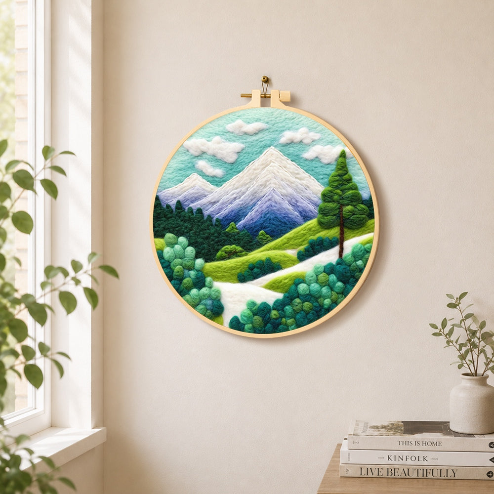 Snow-capped peaks and green trees needle felt wall art displayed in a bright home interior