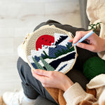 Creating handmade snowy mountain landscape with pine trees and red sun punch needle artwork
