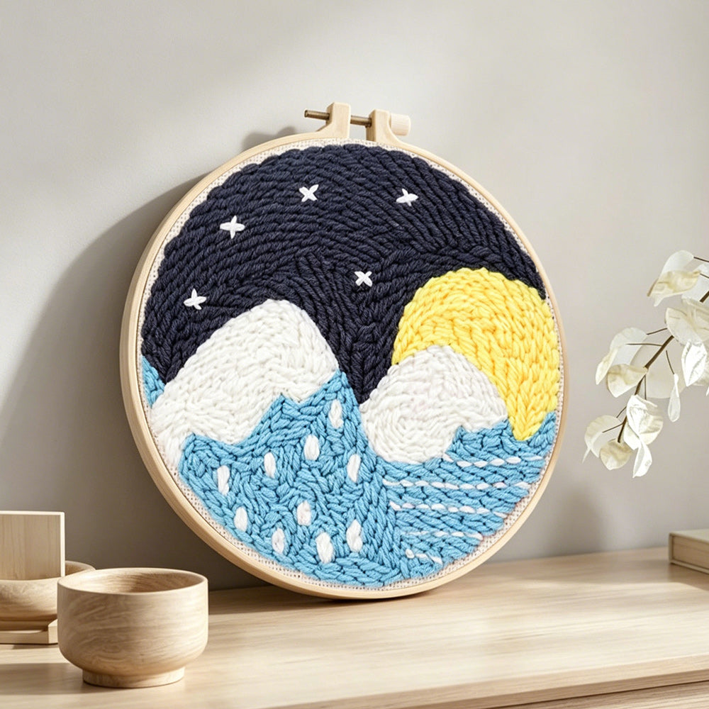 Snowy mountains and blue water under starry sky punch needle artwork displayed on a table
