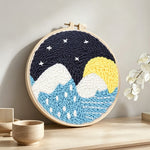 Snowy mountains and blue water under starry sky punch needle artwork displayed on a table
