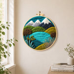 Snowy mountains and summer hills needle felt wall art displayed in a bright home interior