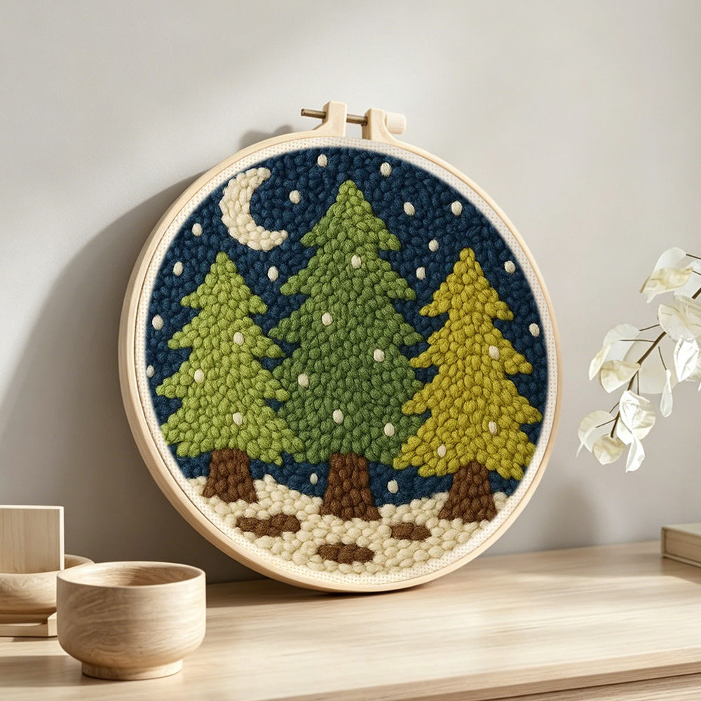 Snowy pine trees and crescent moon punch needle artwork displayed on a table