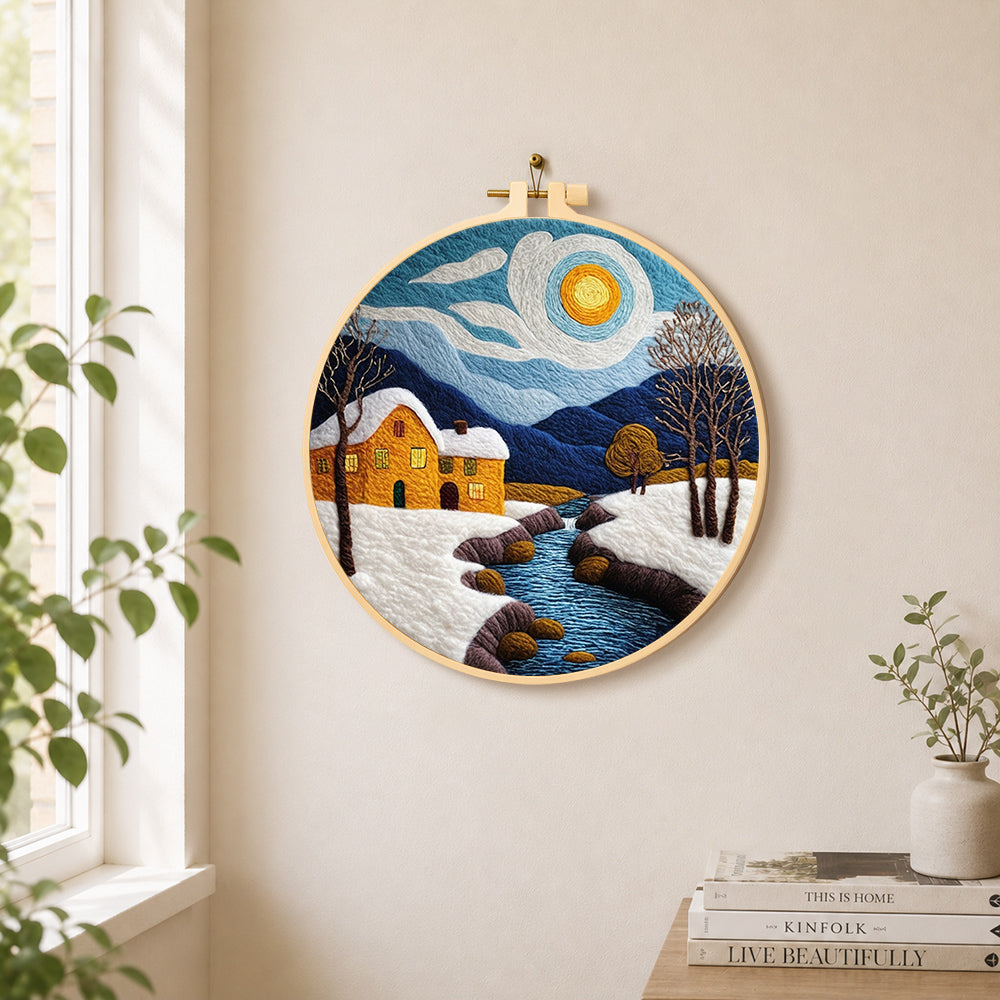 Snowy stream and yellow cottage needle felt wall art displayed in a bright home interior