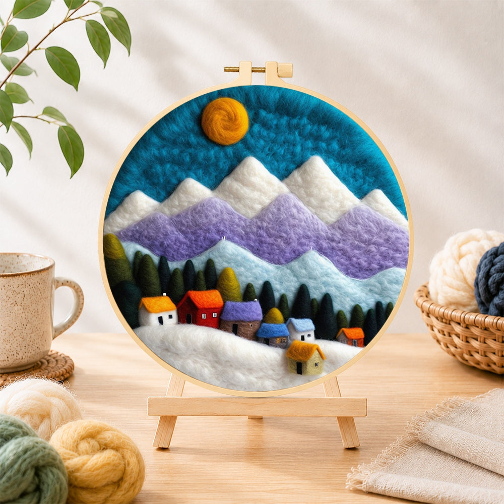 Finished snowy village under the mountains needle felting displayed on a wooden easel