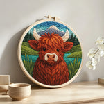 Springtime highland cow and mountain lake punch needle artwork displayed on a table