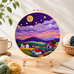 Finished starlit purple mountain village needle felting displayed on a wooden easel