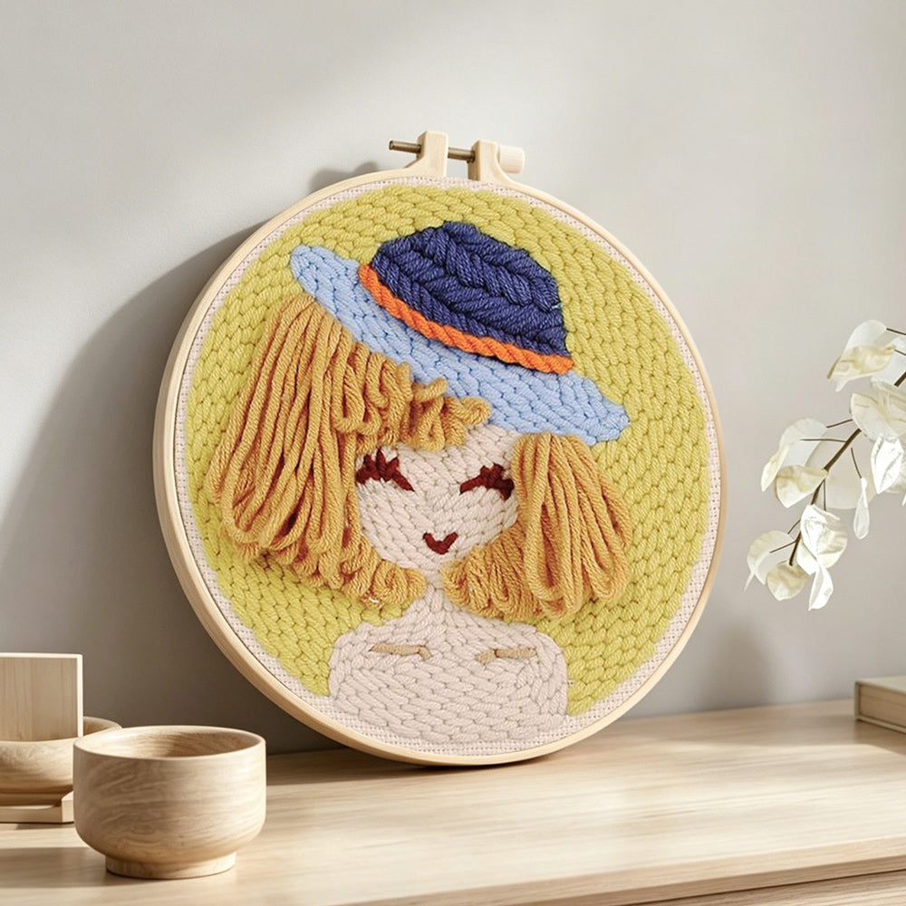 Stylised girl in blue bucket hat punch needle artwork displayed on a table