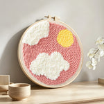 Sun and clouds in pink sky punch needle artwork displayed on a table