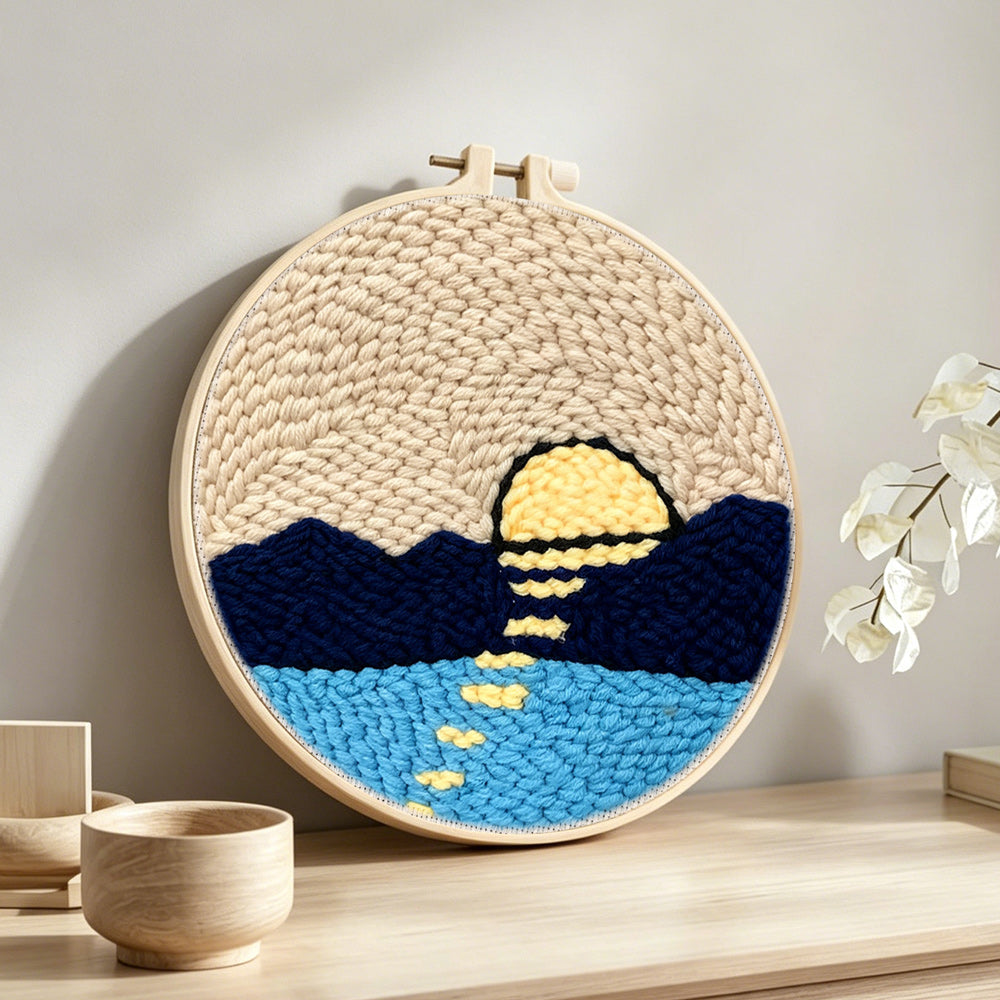 Sun over mountains and water punch needle artwork displayed on a table