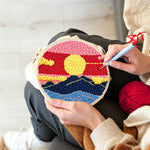 Creating handmade sun over mountains with pink and red sky punch needle artwork