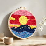 Sun over mountains with pink and red sky punch needle artwork displayed on a table