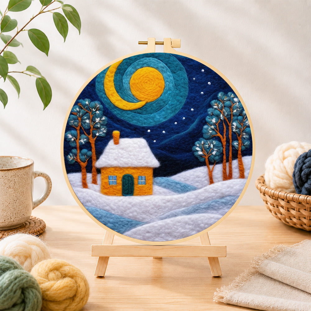 Finished swirling blue sky and yellow snowy cottage needle felting displayed on a wooden easel