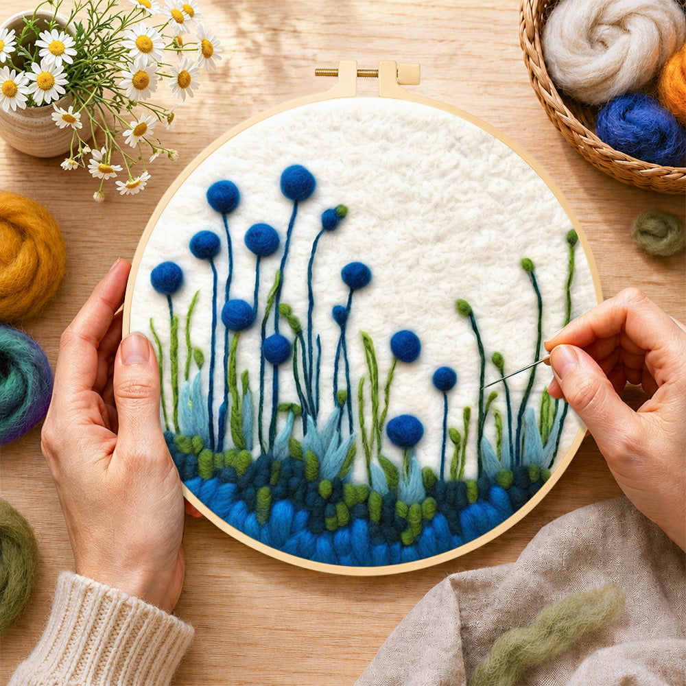 Creating the tall blue wildflowers on white wool painting by hand with a felting needle