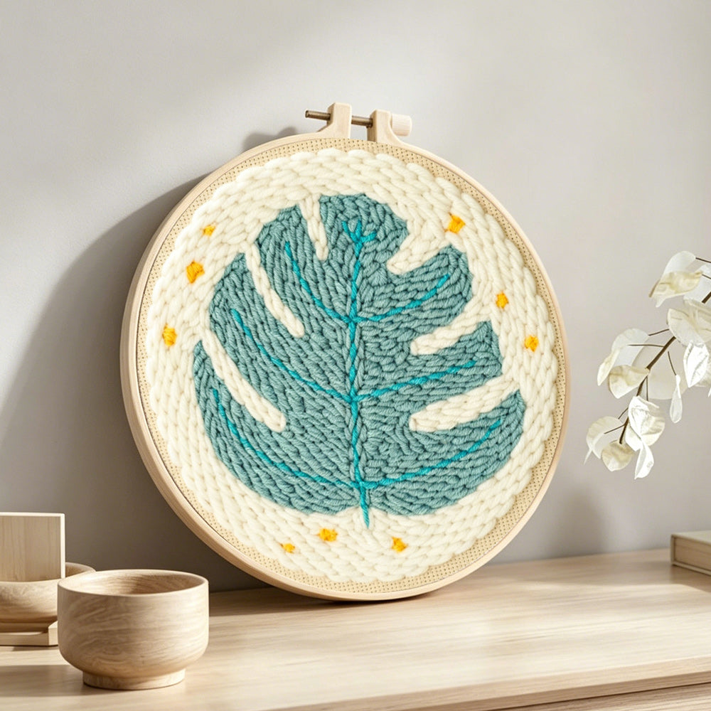 Teal monstera leaf with stars punch needle artwork displayed on a table