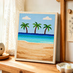 Three palm trees and blue ocean punch needle artwork displayed on a table