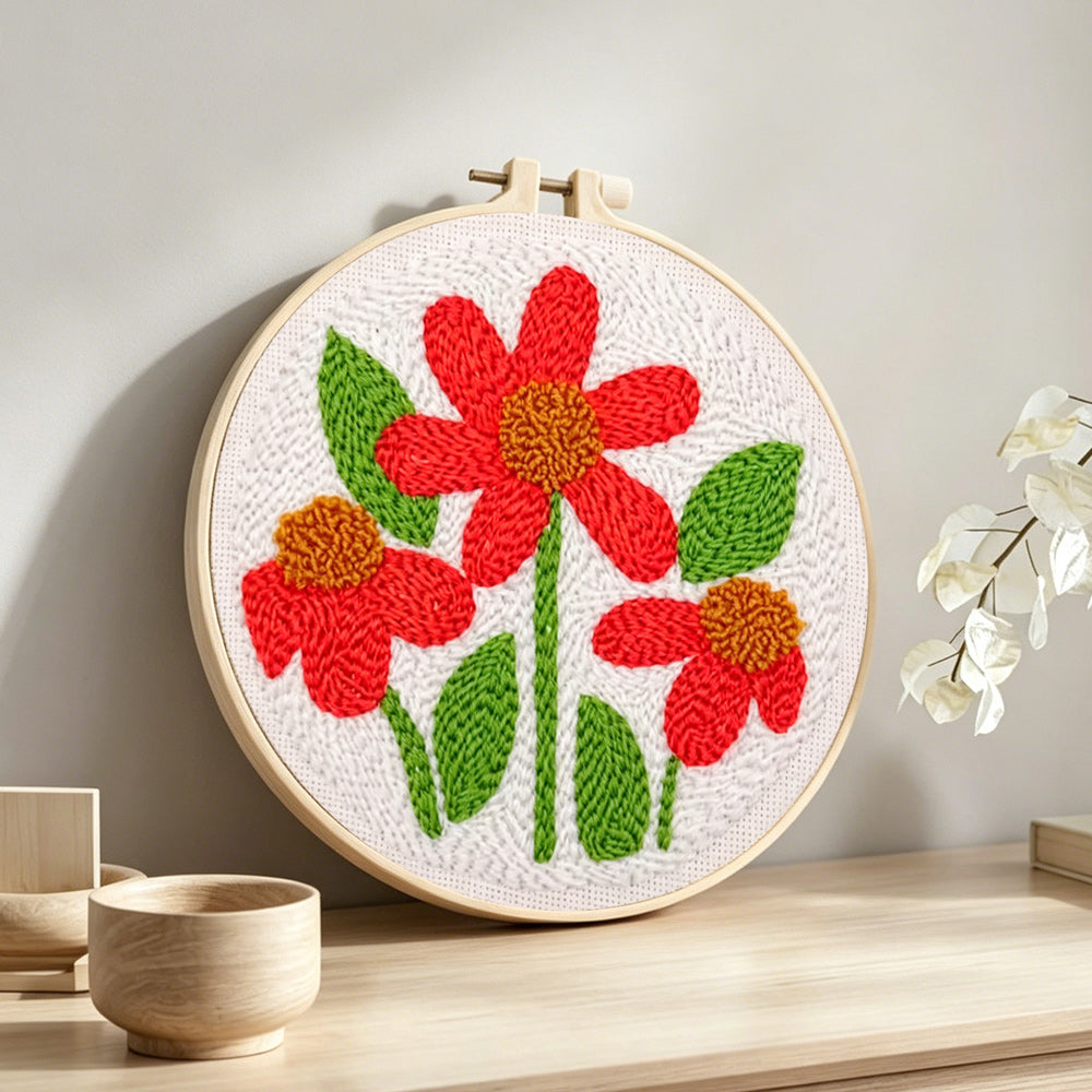 Three red flowers with green leaves punch needle artwork displayed on a table