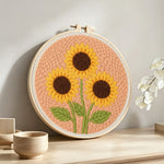 Three sunflowers on peachy pink punch needle artwork displayed on a table