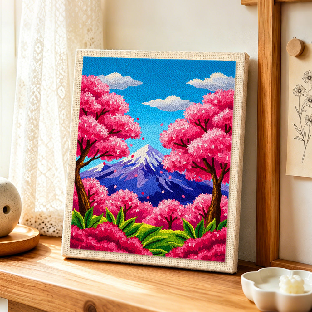 Vibrant cherry blossom trees and snowy peak punch needle artwork displayed on a table