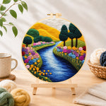 Finished vibrant rolling hills, sunny river and rainbow flowers needle felting displayed on a wooden easel