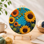 Finished vibrant sunflowers on blue needle felting displayed on a wooden easel