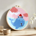 Whale carrying a small house in dreamy sky punch needle artwork displayed on a table