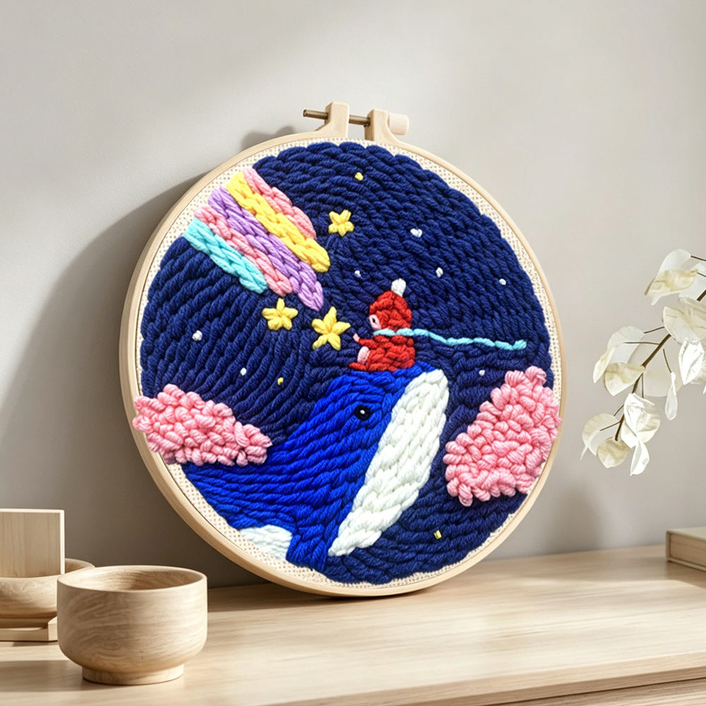 Whale in night sky with rainbow and clouds punch needle artwork displayed on a table