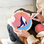 Creating handmade whale jumping in pink sky punch needle artwork