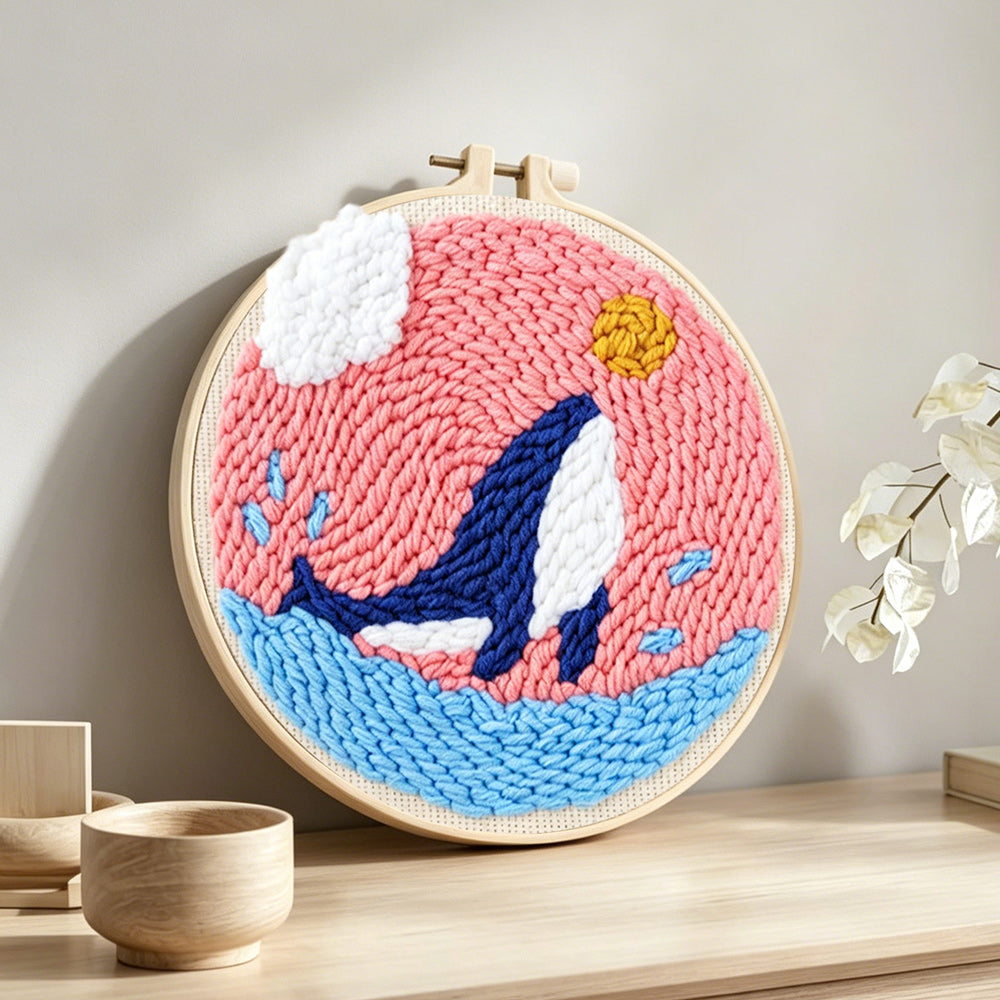 Whale jumping in pink sky punch needle artwork displayed on a table