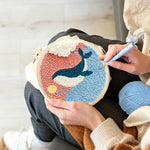 Creating handmade whale jumping out of ocean in pink sky punch needle artwork