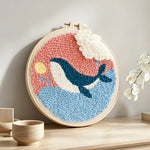Whale jumping out of ocean in pink sky punch needle artwork displayed on a table
