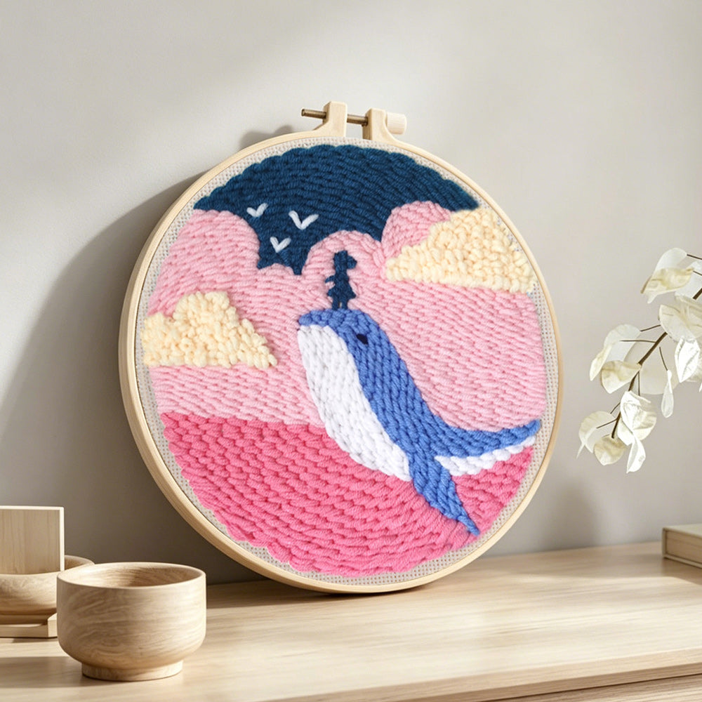 Whale jumping out of pink ocean punch needle artwork displayed on a table