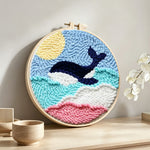Whale jumping over rainbow waves punch needle artwork displayed on a table
