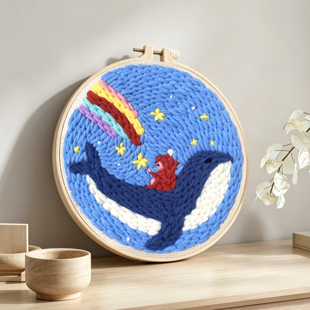 Whale riding astronaut with rainbow sky punch needle artwork displayed on a table